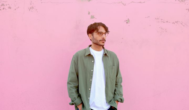 A picture of the artist Babak Ahteshamipour, wearing a white t-shirt and a green overshirt, against a pink background.