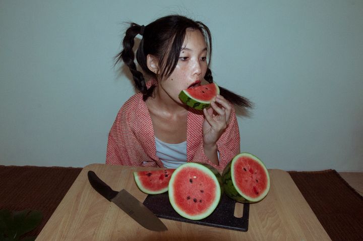A picture of the artist Sabiwa, sat at a table eating watermelon.
