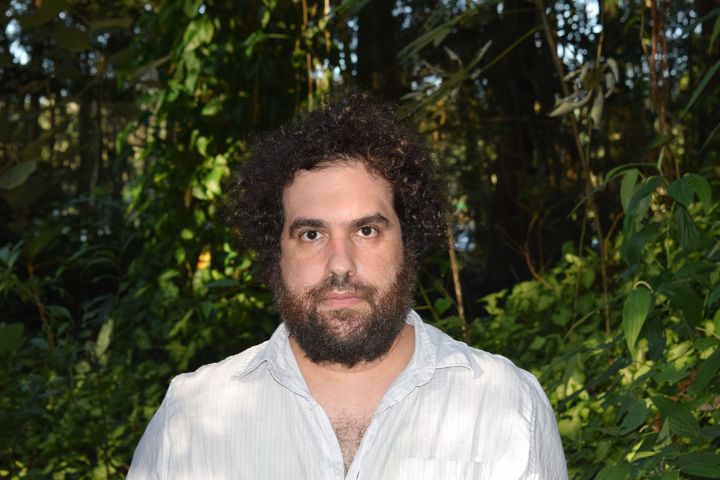 A photo of the artist Babe, Terror, in a white shirt, with trees and foliage in the backgroun